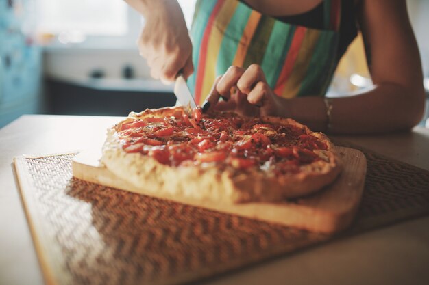 Mujer joven con un cuchillo corta la pizza