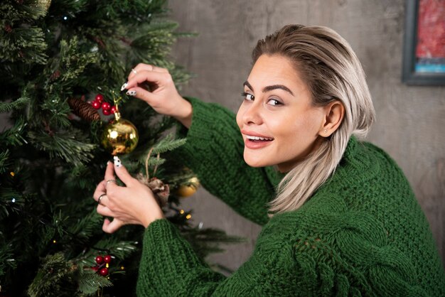 Una mujer joven cuelga un juguete de árbol de Navidad en una rama de un abeto