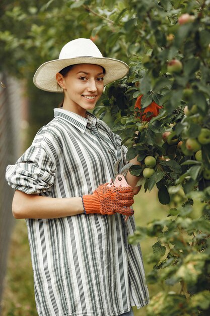 Mujer joven cuidando plantas. Morena con sombrero y guantes. Mujer usa aveeuncator.