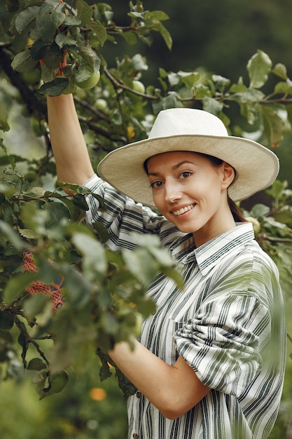 Mujer joven cuidando plantas. Morena con sombrero y guantes.