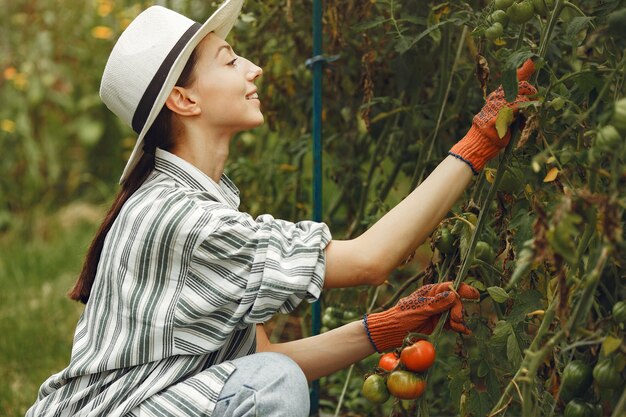 Mujer joven cuidando plantas. Morena con sombrero y guantes.