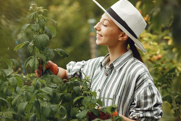 Mujer joven cuidando plantas. Morena con sombrero y guantes.
