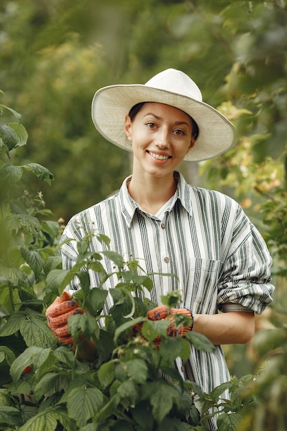 Mujer joven cuidando plantas. Morena con sombrero y guantes.