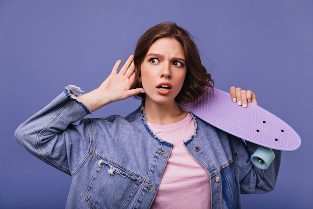 Mujer joven curiosa en chaqueta de mezclilla escuchando. adorable chica rizada posando.