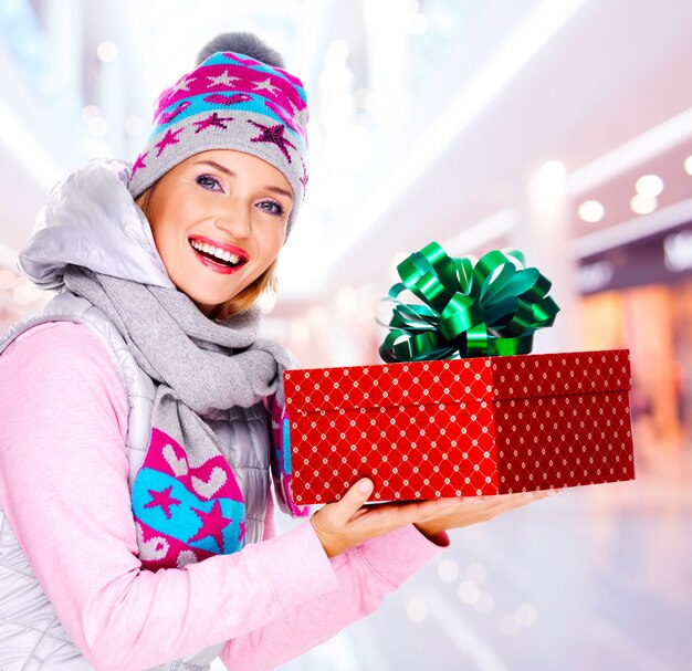 Mujer joven da el regalo de Navidad vestida con una ropa de abrigo de invierno - en el interior