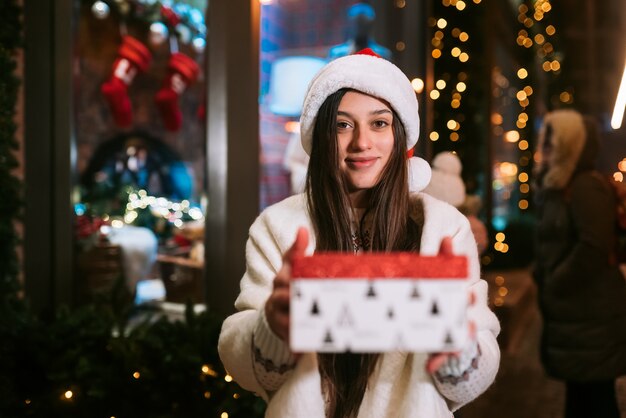 Mujer joven dando caja para usted al aire libre en la calle de invierno Concepto de intercambio de regalos.