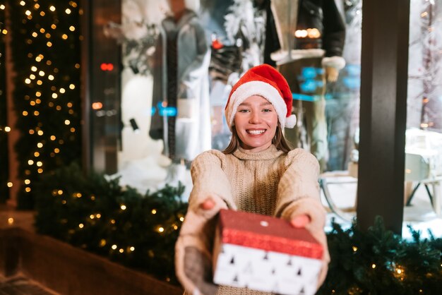 Mujer joven dando caja para usted al aire libre en la calle de invierno Concepto de intercambio de regalos.