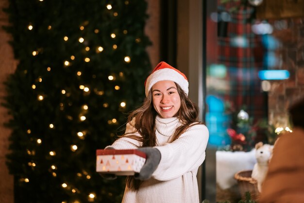 Mujer joven dando caja para usted al aire libre en la calle de invierno Concepto de intercambio de regalos.