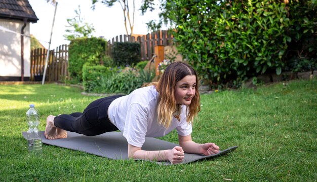 Una mujer joven se dedica a la aptitud en una alfombra en el primer plano de un tablón de la naturaleza