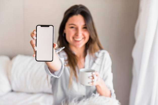 Mujer joven Defocused que muestra el teléfono móvil blanco de la pantalla en blanco