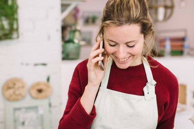 Foto gratuita mujer joven en delantal hablando en teléfono inteligente