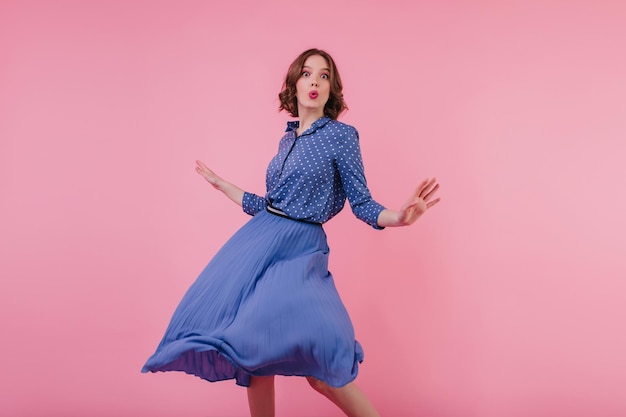 Mujer joven delgada en falda midi azul jugando en el estudio Modelo femenino elegante bailando con expresión de cara de beso sobre fondo rosa