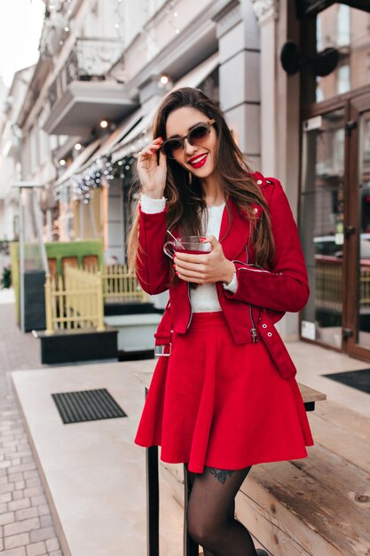 Mujer joven delgada en falda roja posando con sonrisa encantadora en la calle