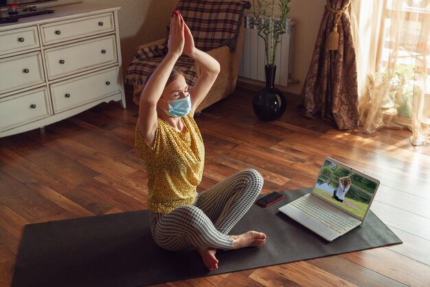 Mujer joven deportiva que toma lecciones de yoga en línea y practica en casa mientras está en cuarentena.