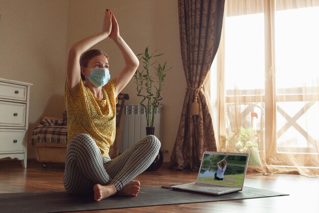Mujer joven deportiva que toma lecciones de yoga en línea y practica en casa mientras está en cuarentena.