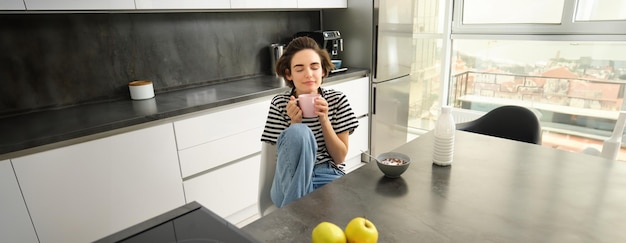 Mujer joven desayunando o almorzando comiendo cereales con leche bebiendo té caliente sentada cómodamente en el