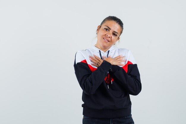 Mujer joven descansando las manos sobre el pecho en suéter y jeans negros y luciendo bonita. vista frontal.