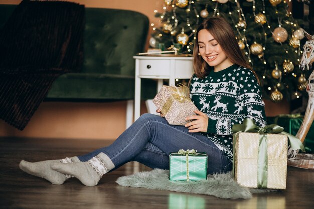 Mujer joven desempacando el regalo de Navidad junto al árbol de Navidad