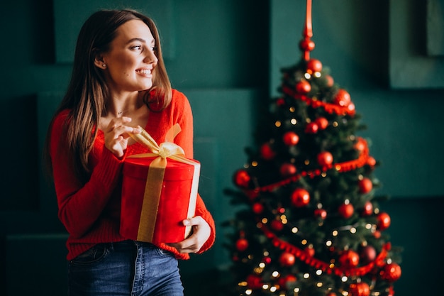Mujer joven desempacando el regalo de Navidad junto al árbol de Navidad