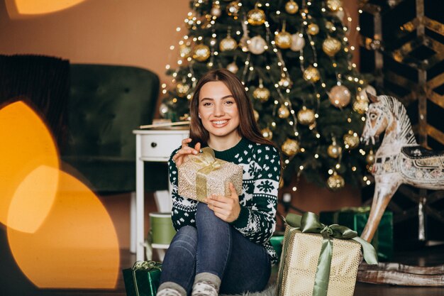 Mujer joven desempacando el regalo de Navidad junto al árbol de Navidad