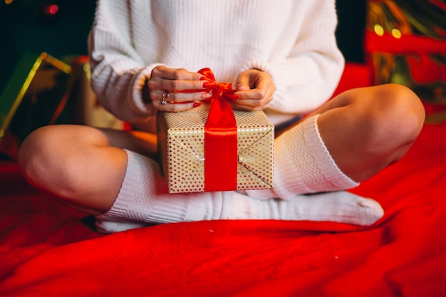 Mujer joven desempaquetando regalos por arbol de navidad