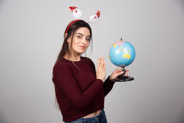 Mujer joven en diadema de Navidad sosteniendo un globo terráqueo.