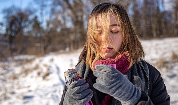 Una mujer joven disfruta de una bebida caliente de un termo en un paseo en invierno