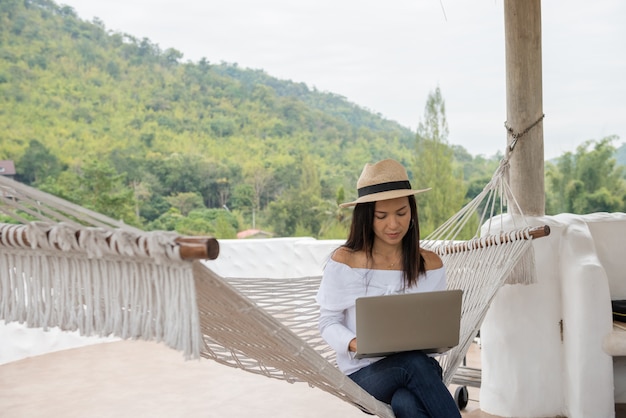 Mujer joven disfruta de una computadora portátil en una hamaca en la playa