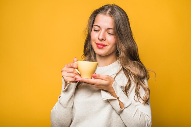 Mujer joven disfruta el olor de su café fresco contra el fondo amarillo
