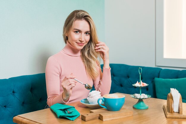 Mujer joven disfrutando del merengue y café capuchino en la cafetería