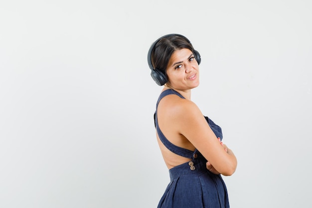 Mujer joven disfrutando de la música con auriculares en vestido y mirando alegre. .