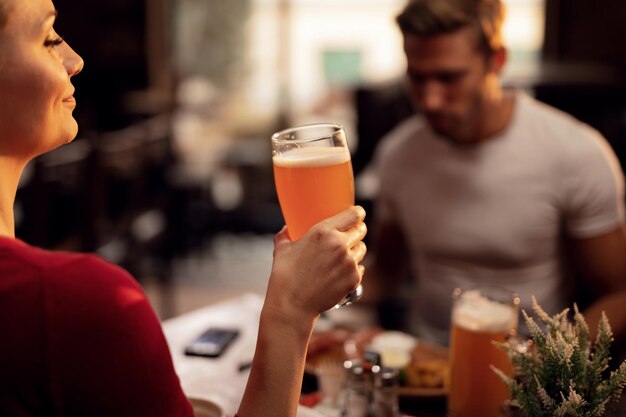 Mujer joven disfrutando en un vaso de cerveza mientras está en un pub con su novio