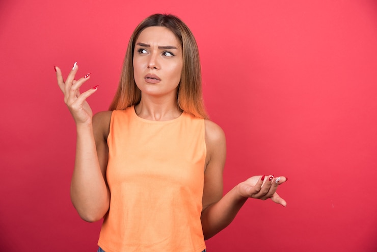 Foto gratuito mujer joven disgustada confundida por algo en la pared roja.