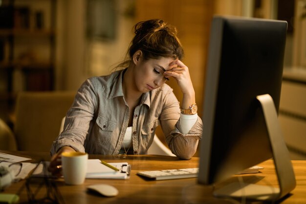 Mujer joven disgustada pensando mientras trabajaba en una PC de escritorio por la noche en casa