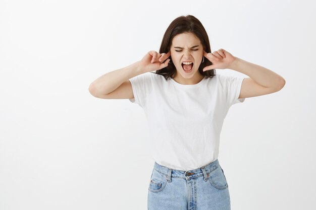 Mujer joven disgustada posando contra la pared blanca