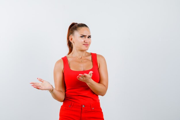 Foto gratuita mujer joven disgustada con una pregunta tonta en camiseta roja, pantalones y mirando perplejo, vista frontal.