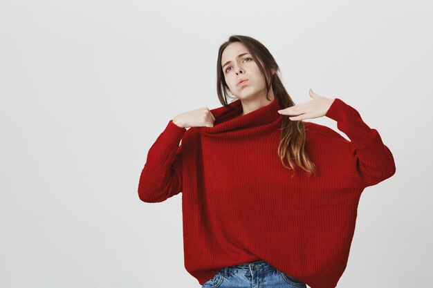Mujer joven disgustada en suéter rojo siente calor, trata de refrescarte