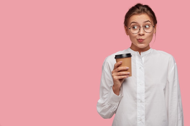 Mujer joven divertida con gafas posando contra la pared rosa