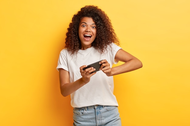 Mujer joven divertida con el pelo rizado posando con su teléfono