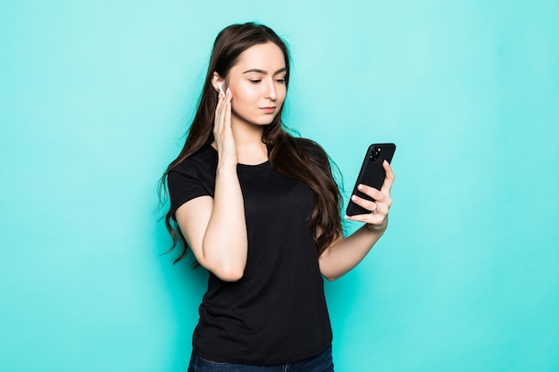 Mujer joven divertida en sudadera con capucha blanca casual posando aislada en el retrato de la pared azul turquesa. Concepto de estilo de vida de personas. Burlarse del espacio de la copia. Escuche música con cápsulas de aire, manteniendo los ojos cerrados