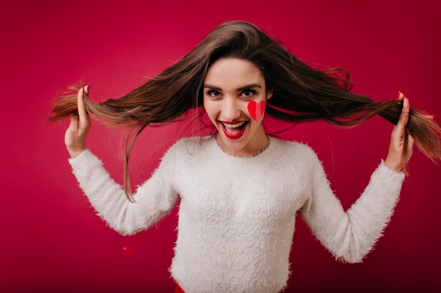 Mujer joven divertida en suéter esponjoso posando en el día de San Valentín con sonrisa