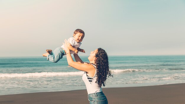 Mujer joven divirtiéndose con el bebé en la playa de verano