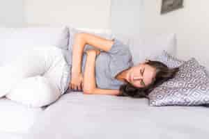 Foto gratuita mujer joven con dolor abdominal debido a la menstruación acostada en el sofá y sosteniendo su estómago.