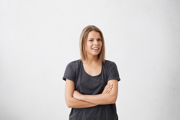 Foto gratuita mujer joven dudosa e insatisfecha que tiene mirada escéptica y suspicaz, mantiene los brazos cruzados, expresa sospecha o duda. actitud, reacción y emociones humanas