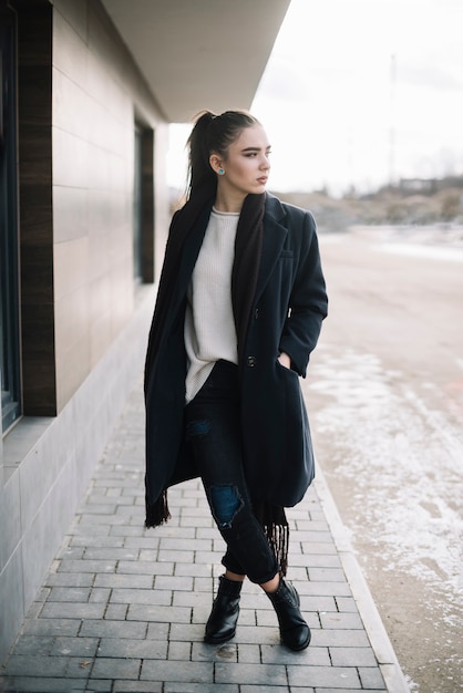 Mujer joven elegante en capa con la bufanda en la calle