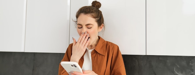 Foto gratuita mujer joven y elegante en casa mirando la pantalla del móvil bostezando mientras lee un mensaje