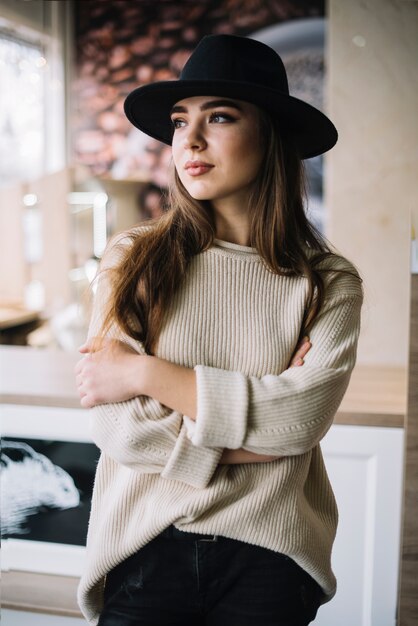 Mujer joven elegante pensativa en sombrero con las manos cruzadas