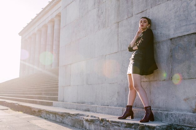 Mujer joven elegante que se coloca en pared con luz del sol