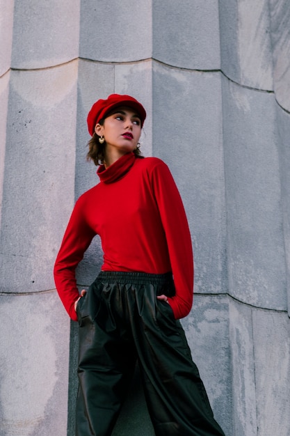 Mujer joven elegante que lleva el casquillo rojo con las manos en su bolsillo que mira lejos