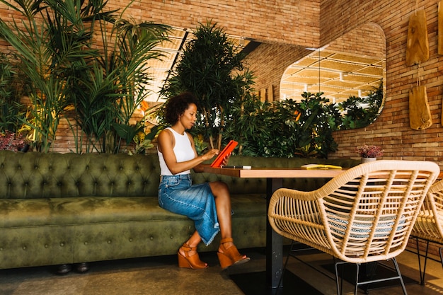 Mujer joven elegante que usa la tableta digital en la mesa del restaurante